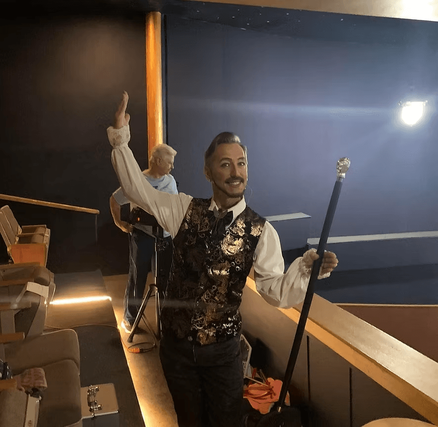 Dr. Jakey in a gold brocade vest, cane raised, in the balcony